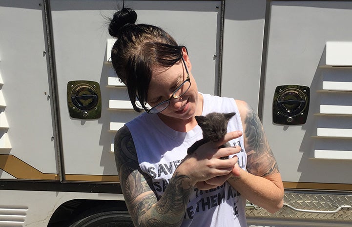 Jenn Stone holding a small gray kitten in front of an RV