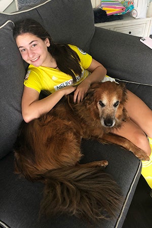 Girl wearing a sports outfit sitting on the couch with Tate the dog