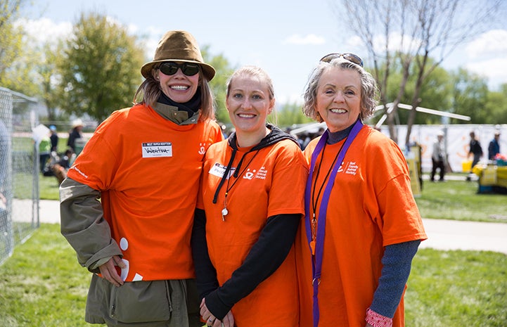 Three female volunteers wearing bright orange T-shirts posing together