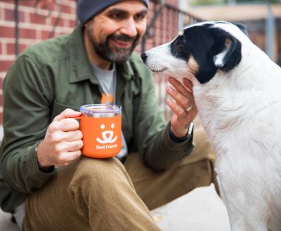 Smiling person enjoying a cup of coffee while sitting next to their dog outside