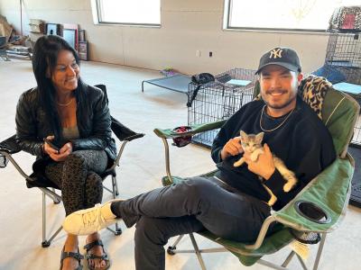 Lillian the kitten being held by her adopter sitting in a chair, next to another person sitting in another chair