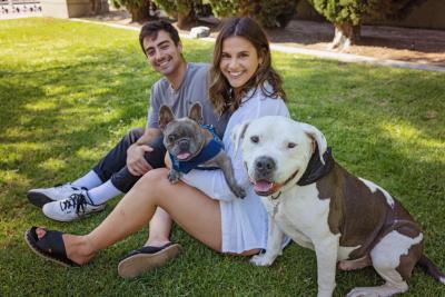 Alyssa Leon and Tommy Rigdon sitting in some grass with their two adopted dogs, Brew and Julien