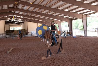 Christian Mathews riding Byron the mustang while holding a large blue and yellow ball