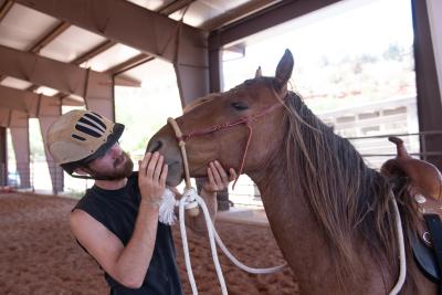 Christian Mathews wearing a helmet and petting the face of Byron the mustang horse