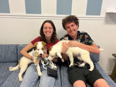 Two people sitting on a couch smiling and holding two puppies at the National Adoption Weekend