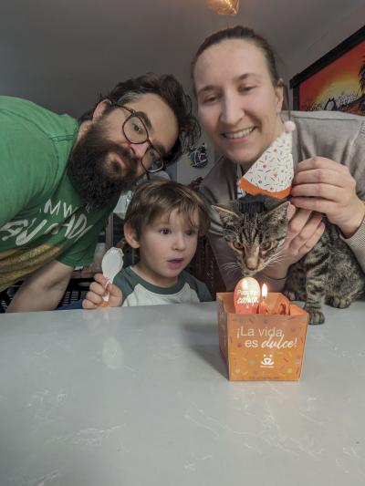 Nosferatu the cat wearing an adoption hat by his adoption cake with his family