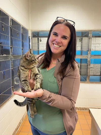 Smiling person holding a tabby cat in front of some cat kennels