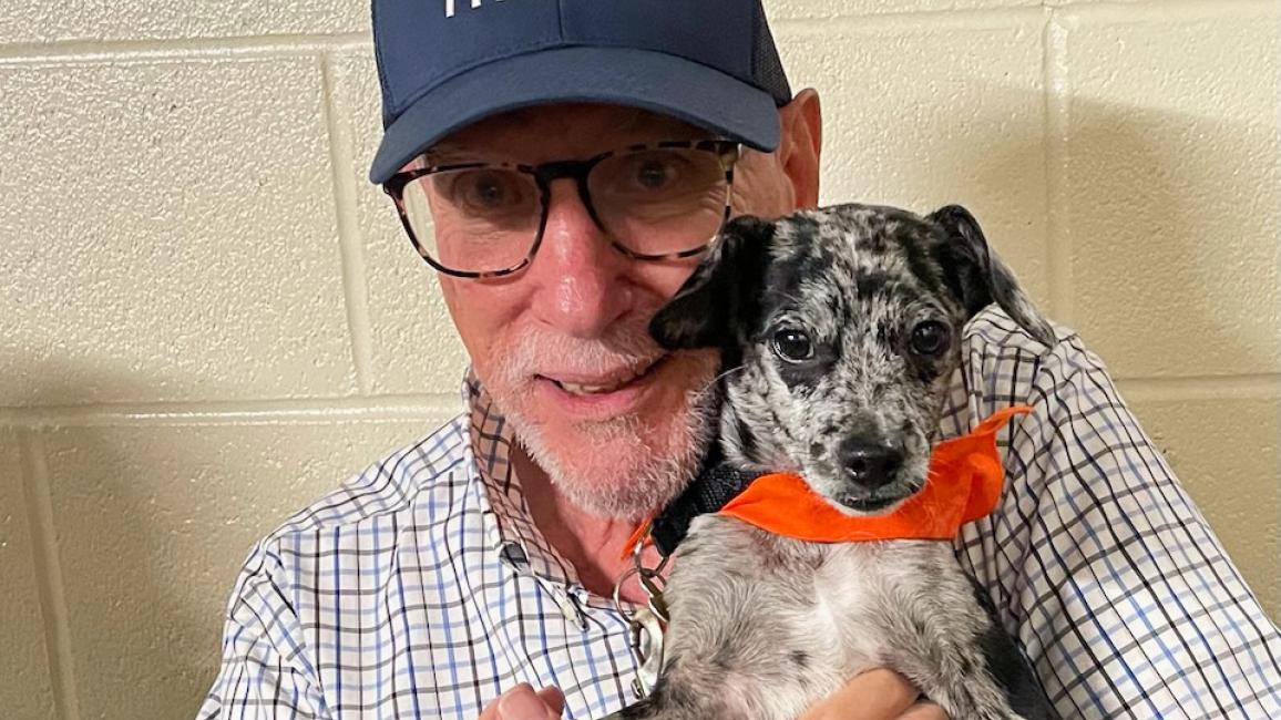 Ira Shankman wearing a Best Friends hat and holding Sonny the puppy, who is wearing hos orange bandanna