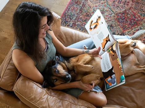 Woman lying on a couch reading a book with dog in her lap