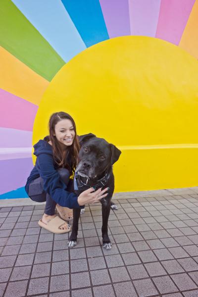 Duke the dog with his new person with a colorful sun mural behind them