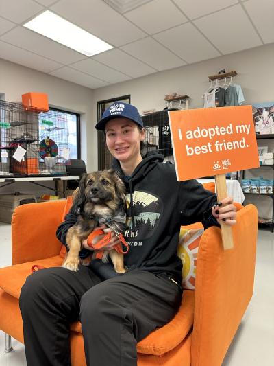 Malt the dog in the lap of Mackenzie, who is holding a sign that says, "I adopted my best friend"