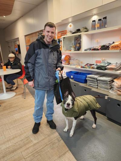 Lucky Charm the dog wearing a coat and on a leash held by his new person