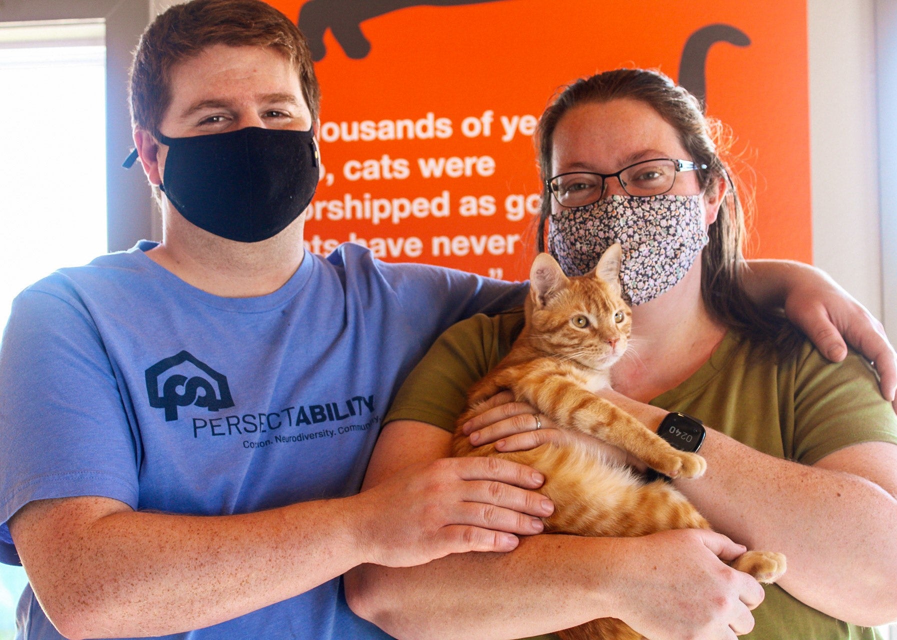 Two people wearing masks holding orange cat