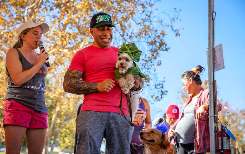 Happy person holding a small dog at an outdoor Strut Your Mutt event