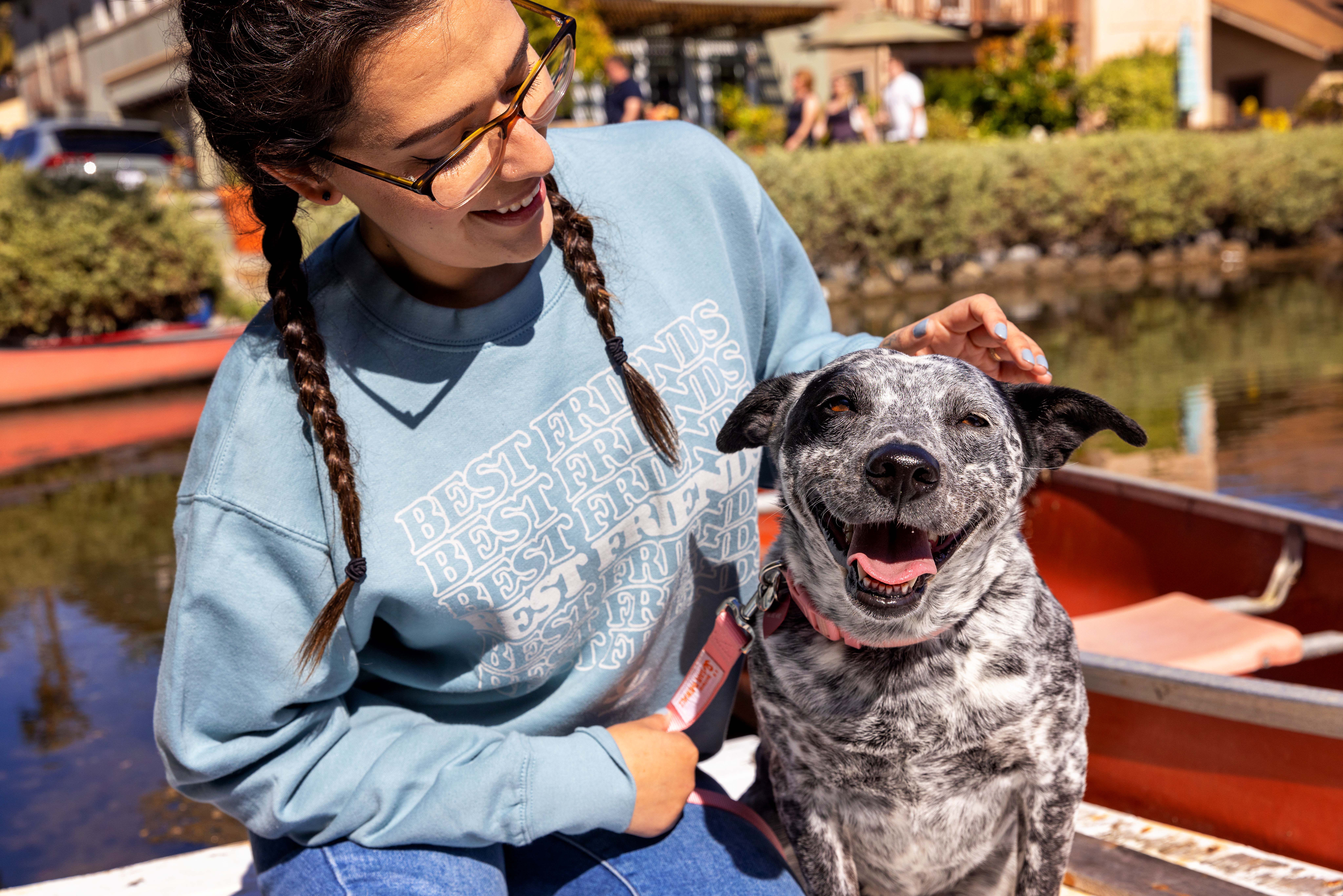 Smiling person wearing braids and a Best Friends sweatshirt petting a happy dog