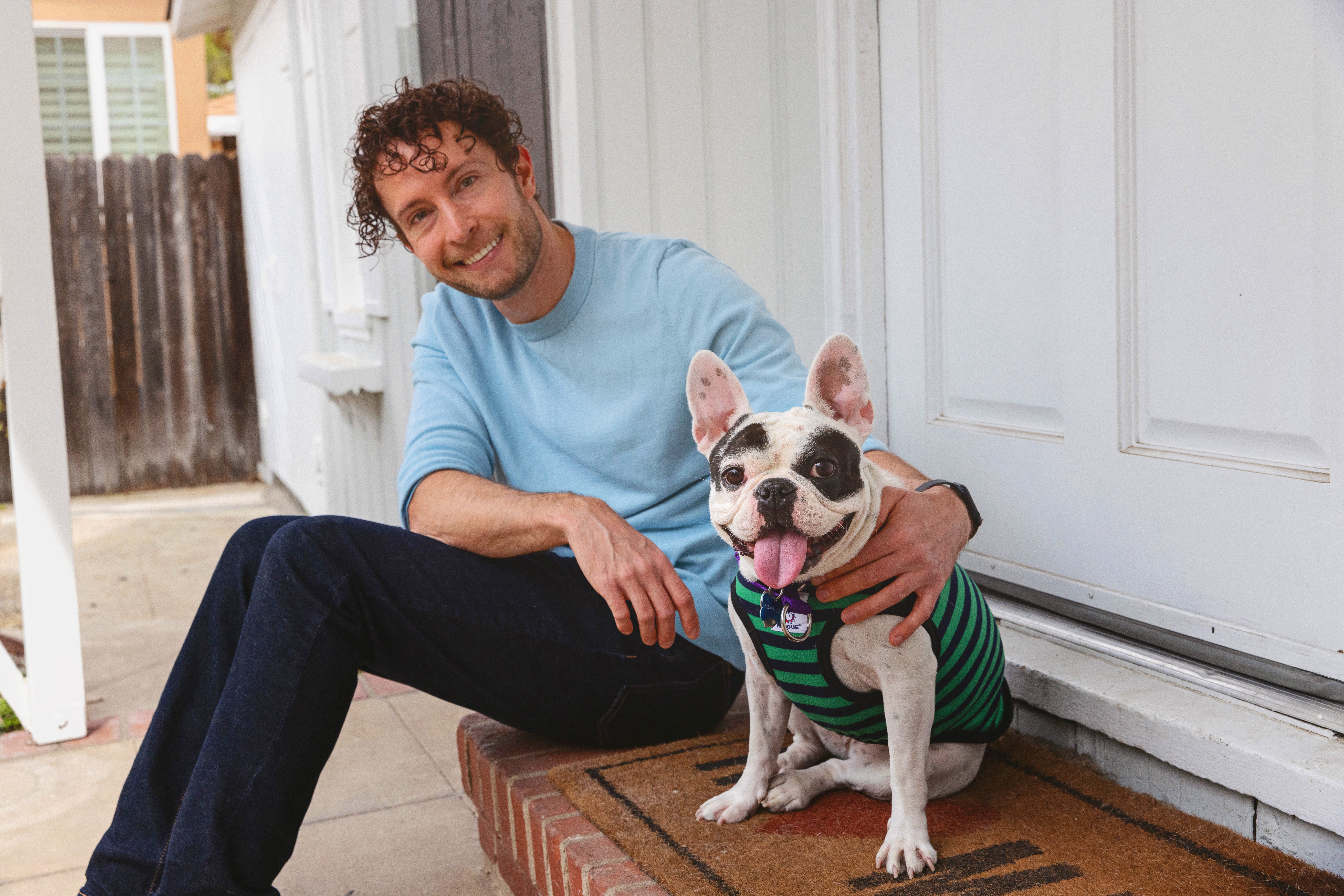 Smiling person sitting outside on some steps with a small dog