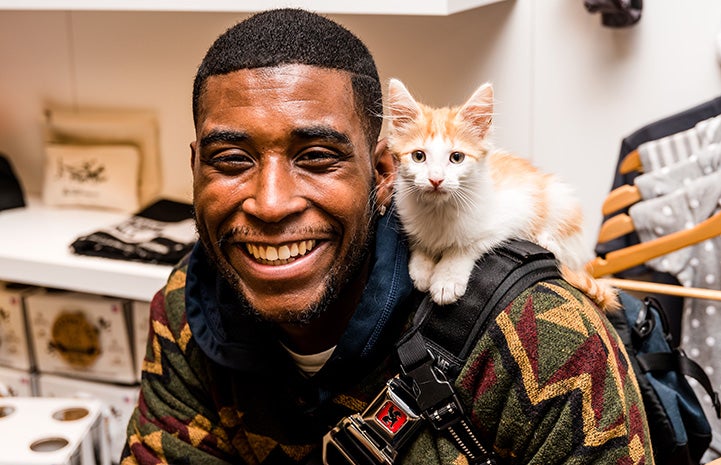 Smiling man with a white and cream colored kitten on his shoulder