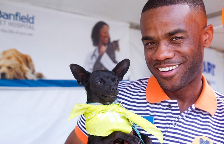 Smiling man holding the small black Chihuahua mix dog who he adopted