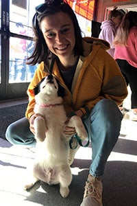 Smiling woman squatting on the ground and holding a black and white puppy up