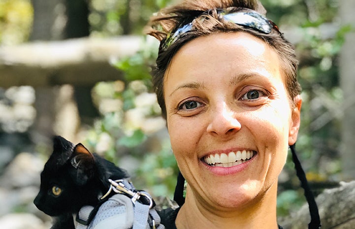 Rafa the kitten in a harness on the shoulder of a smiling woman