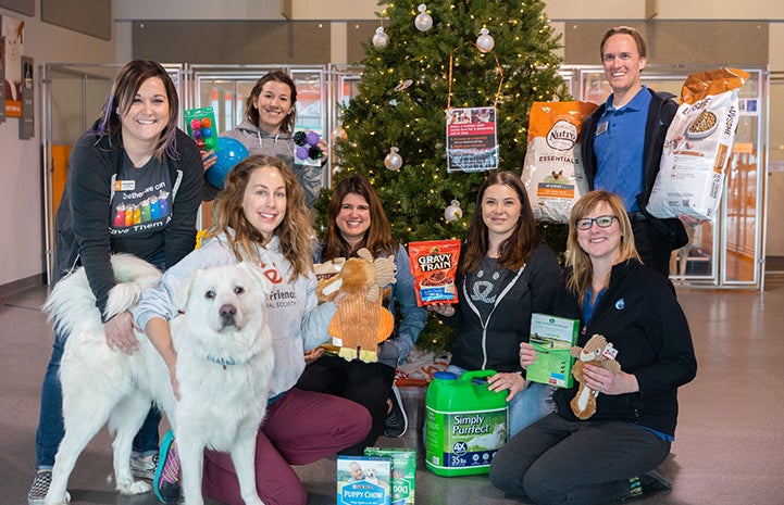 People from the Best Friends Pet Adoption Center in Salt Lake City posing with donations and a dog in front of a Christmas tree