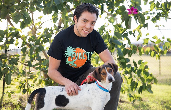 Luis Quintanilla kneeling down and petting a brown and white dog while wearing a PVAC TX T-shirt
