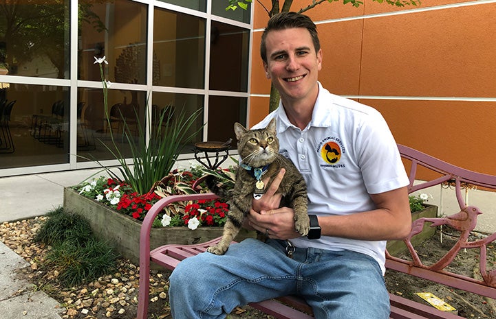 Spencer Conover at Pasco County Animal Services, sitting on a bench holding a brown tabby cat