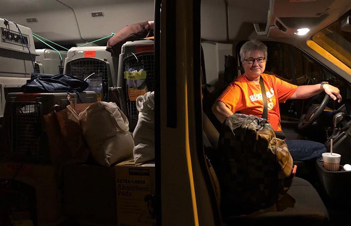 Woman wearing a Best Friends T-shirt in the driver's seat of a transport van full of crates holding animals