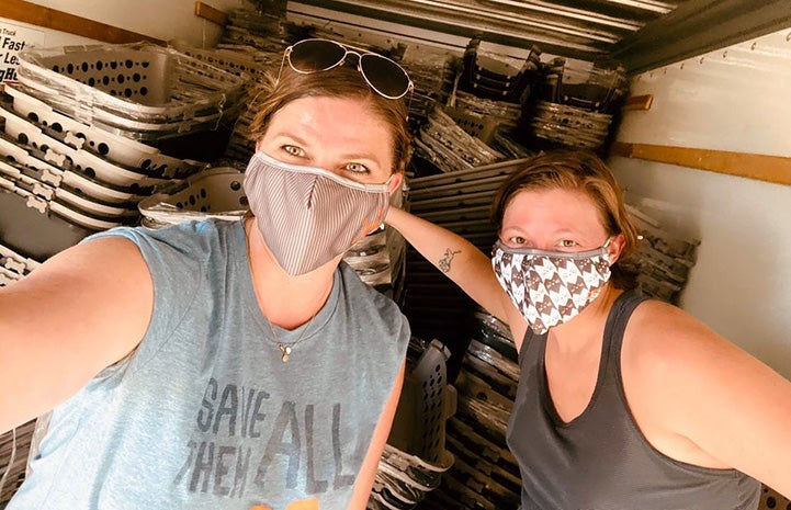 Two masked women standing in front of a huge pile of anima crates