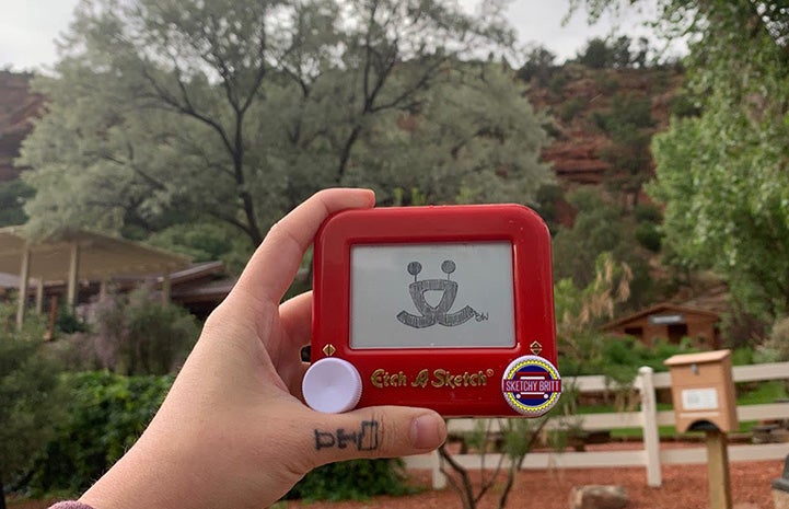 Britt West holding Etch-a-Sketch with Best Friends logo in front of a view of the Welcome Center