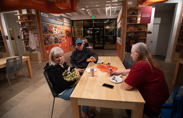 Three people sitting at a table at the Best Friends Roadhouse and Mercantile, with one woman holding Robert Johnson the dog