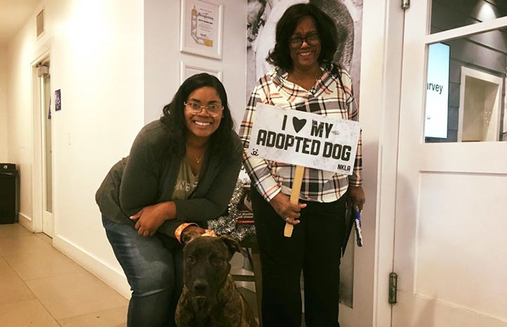 Two women next to Cuba the dog they'd just adopted, holding a sign that says I heart my adopted dog