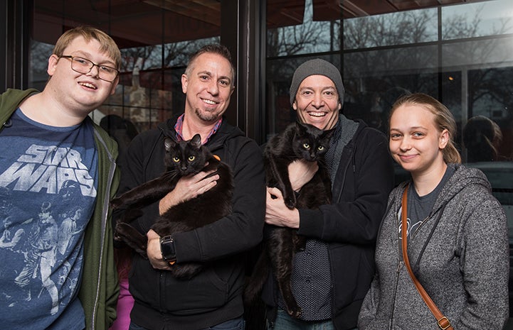 Smiling family holding Orion and Santino, two black cats they just adopted
