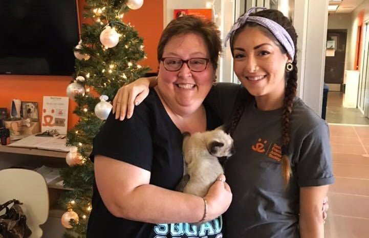 Best Friends employee next to a woman holding Valentino, a Siamese mix kitten she adopted