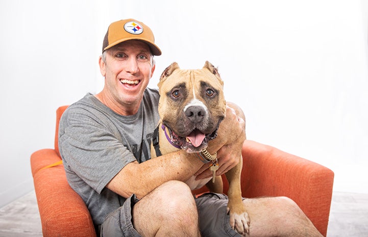 Portrait of volunteer Danny Bress with Beefy the dog sitting together on an orange chair