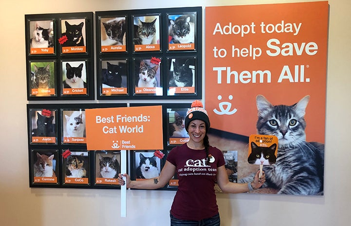 Volunteer Natalie posing with a Best Friends Cat World sign and fan in front of a display at Cat World HQ 
