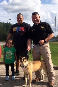 Two men and a child standing with a shepherd type dog on a leash