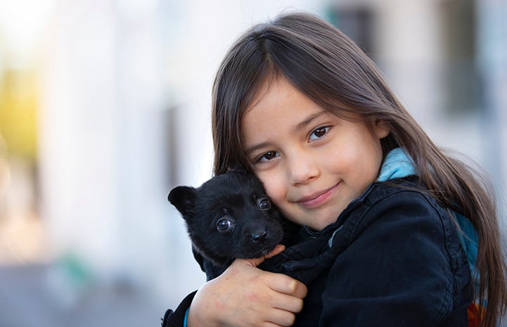 Young girl hugging a small black puppy