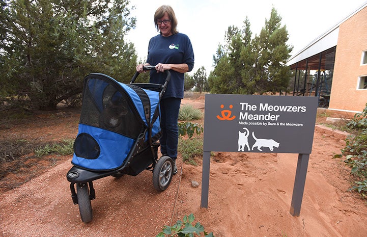 Woman taking a cat on a stroller ride next to a The Meowzers Meadow sign