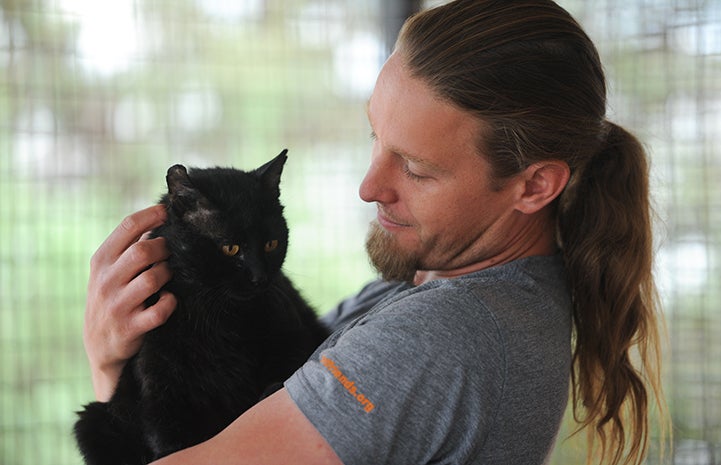 Cat World caregiver Levi Myers cradling a black cat in his arms