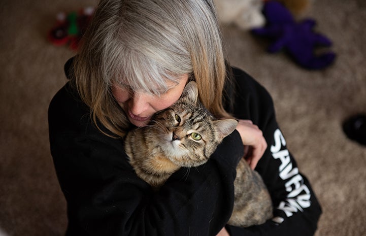 Birdie the tabby cat being held and hugged by the woman who adopted her