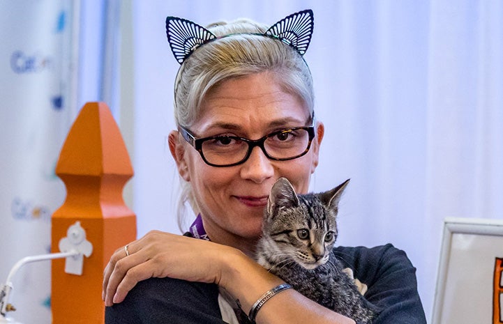 Woman wearing cat ears holding a tabby kitten