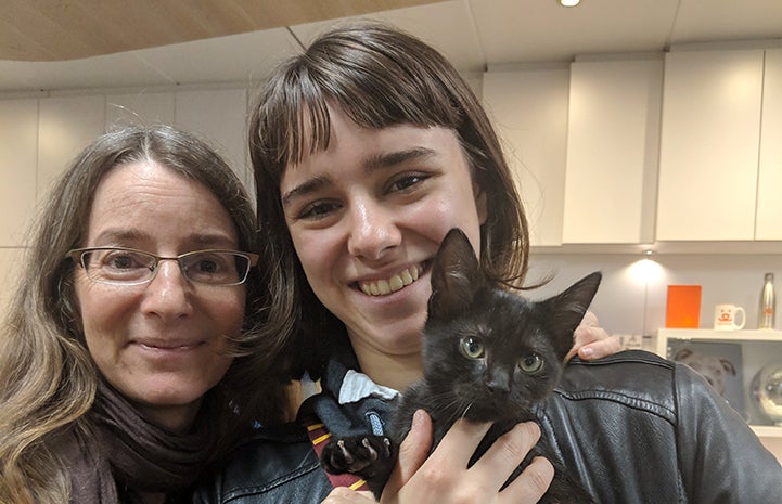 Two smiling women, Chandra and Dorina, holding Jelly the black cat and smiling