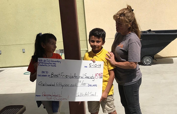 A large check to Best Friends Animal Society being held by a woman and two kids