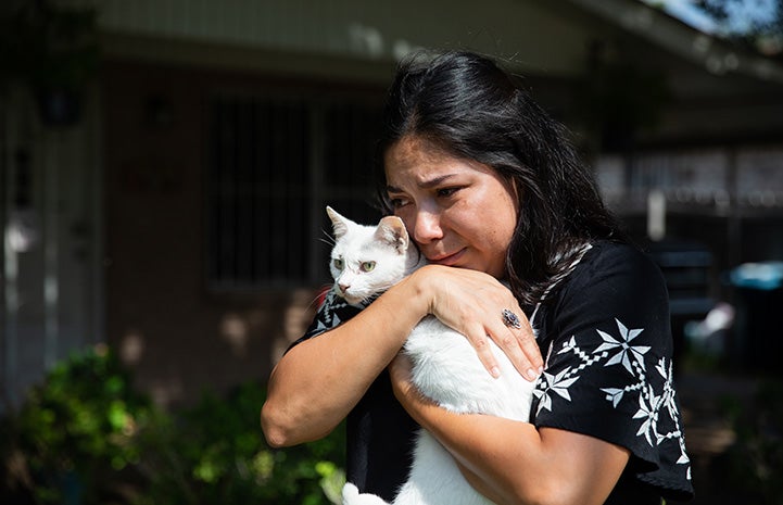 Grateful looking woman cradling a white cat in her arms after being reunited
