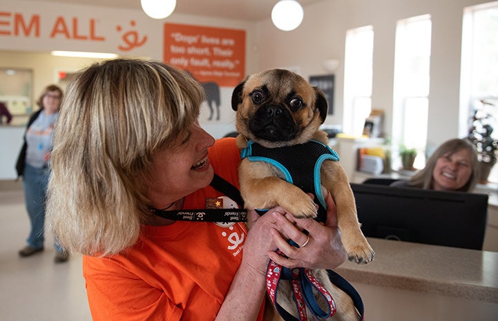 Smiling woman holding Salvador Dogi the pug in the lobby of Dog Headquarters