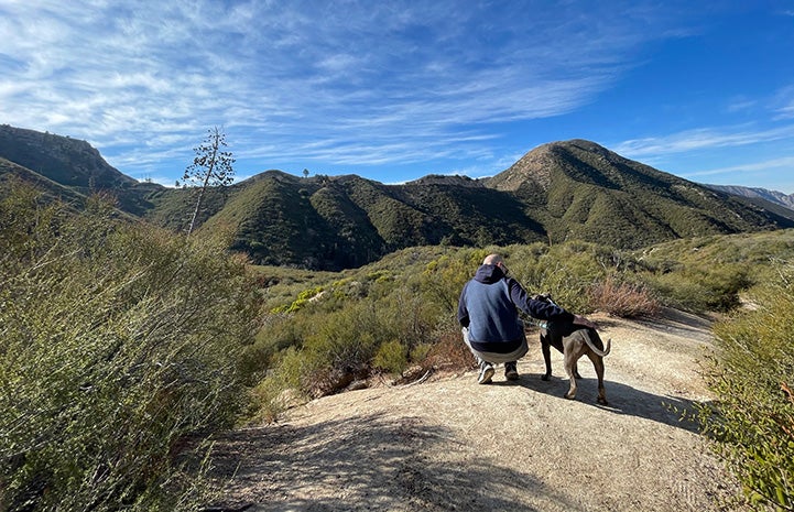 Person and Cannoli the dog on a trail surrounded by hills