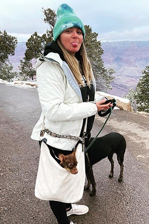 Woman wearing a hat with Molly Brown the dog in her pocket and walking another dog on a leash