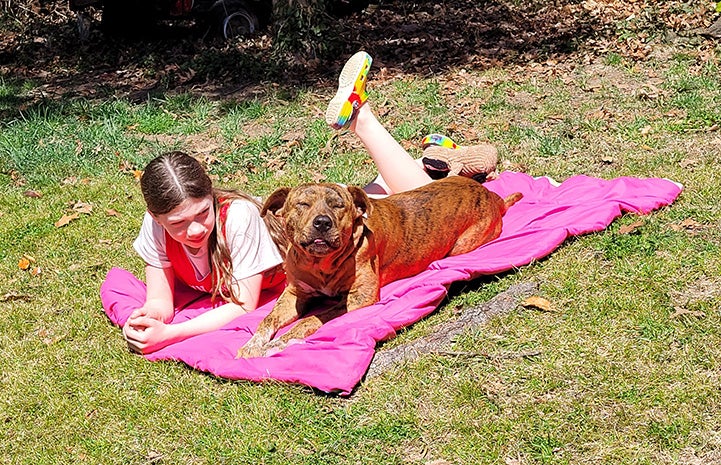 Pancho the dog lying on a pink towel with eyes closed in happiness next to a young girl