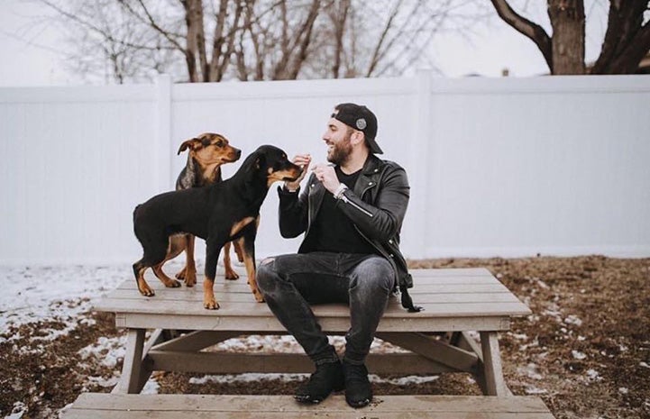 Tyler Rich sitting on the top of a picnic table with two dogs